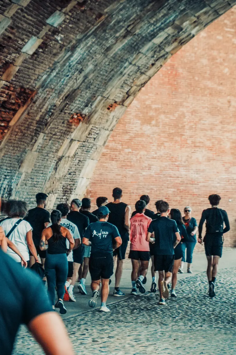 Un peloton de coureurs vu de dos s'engage sous les arches de brique d'un quai toulousain