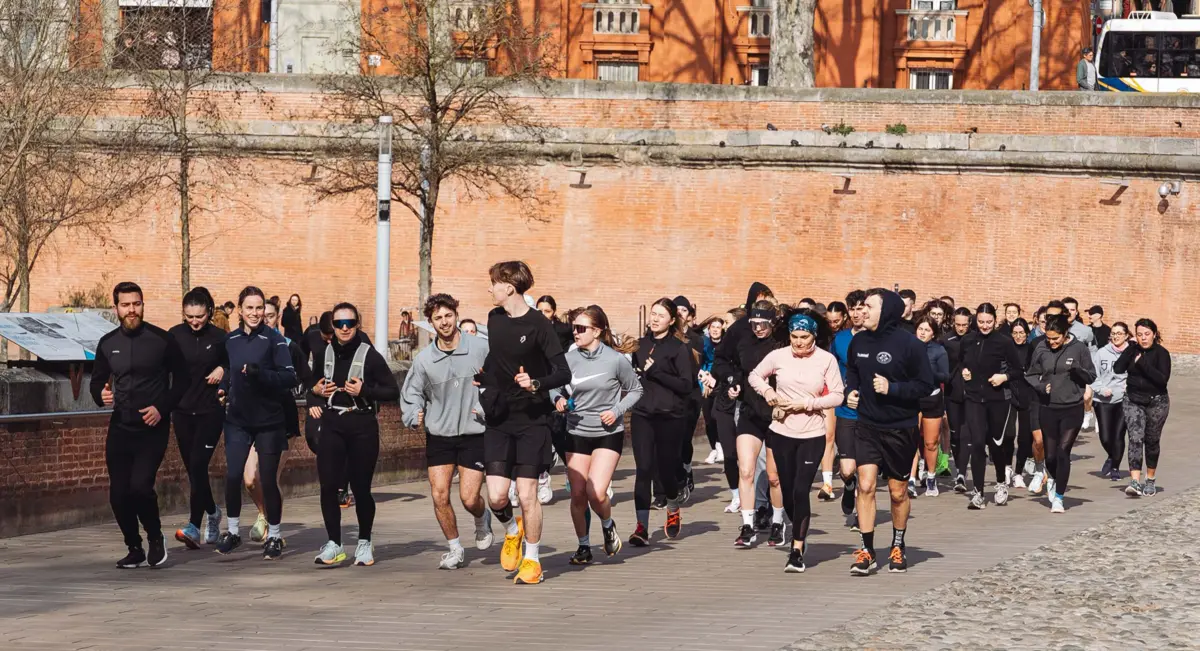 Un peloton de coureurs avance le long d'un rempart de brique rose, à Toulouse